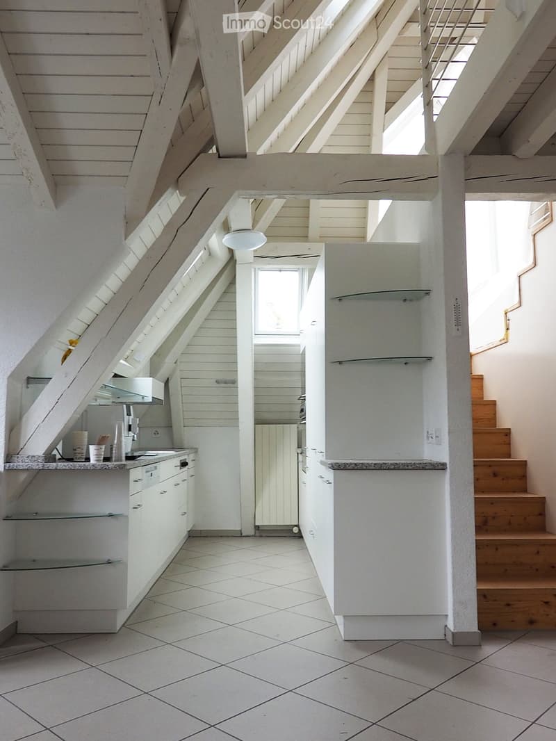 Modern kitchen with white cabinets, granite countertop, and stainless steel appliances. The space features a tiled floor and a staircase leading upwards.