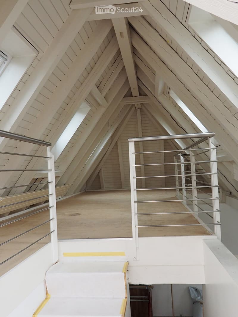 Spacious, open loft area with exposed wooden beams and skylights, featuring a modern metal staircase with white railings leading to an upper level.