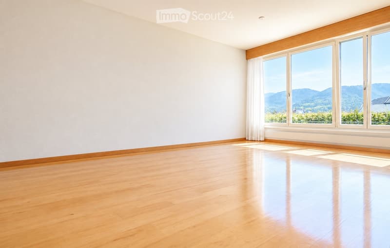 Empty room with wooden flooring, white walls, large windows with white curtains, and a scenic mountain view outside.