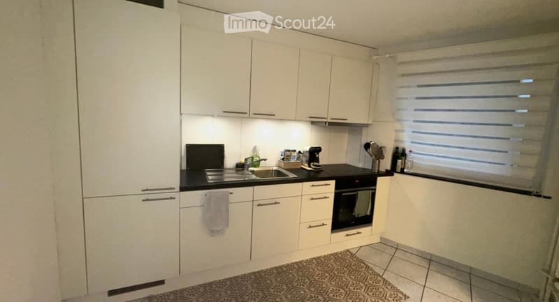 Modern kitchen with white cabinets, black countertops, stainless steel sink, and various appliances including a coffee maker and oven.