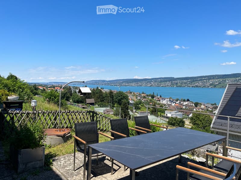 Balcony with a table and chairs, overlooking a scenic lake and cityscape.