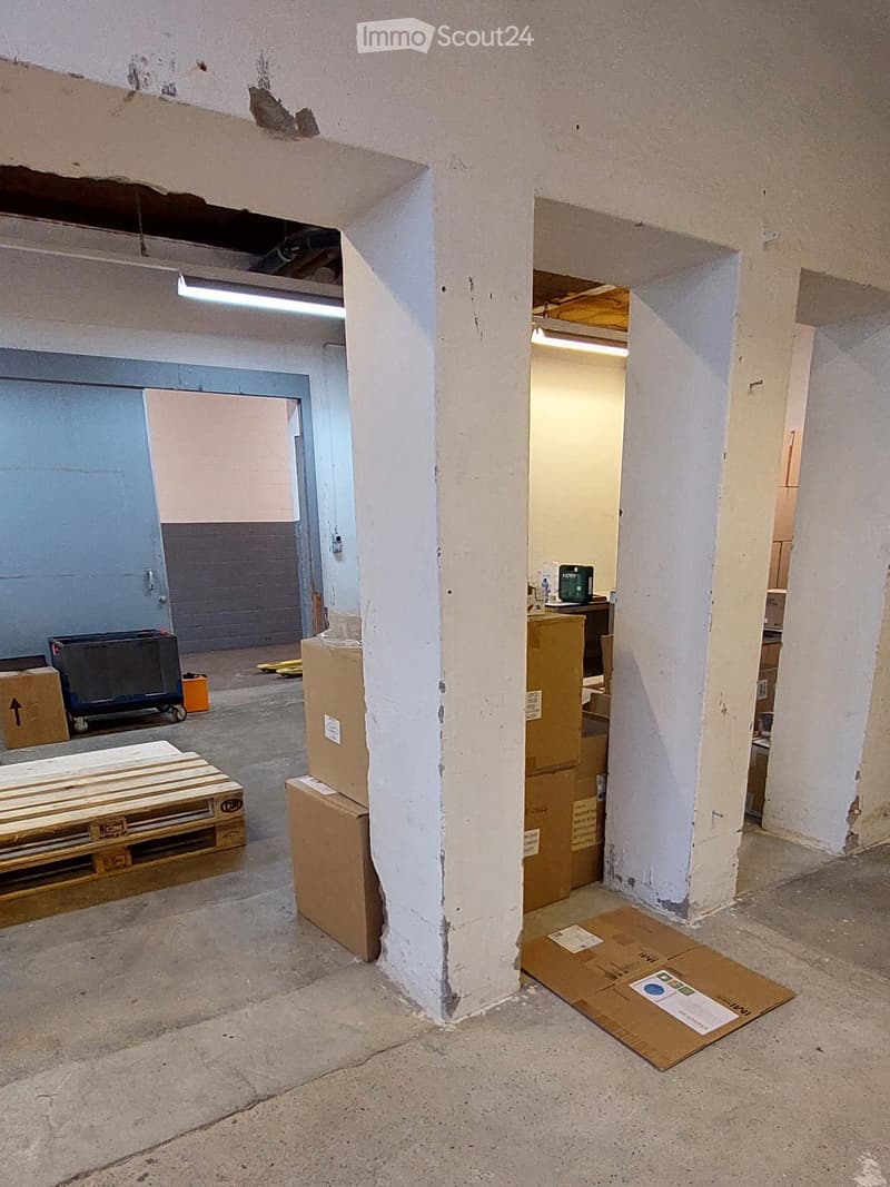 Empty room with exposed concrete floor, white walls, and scattered cardboard boxes and pallets. No furniture or equipment visible.