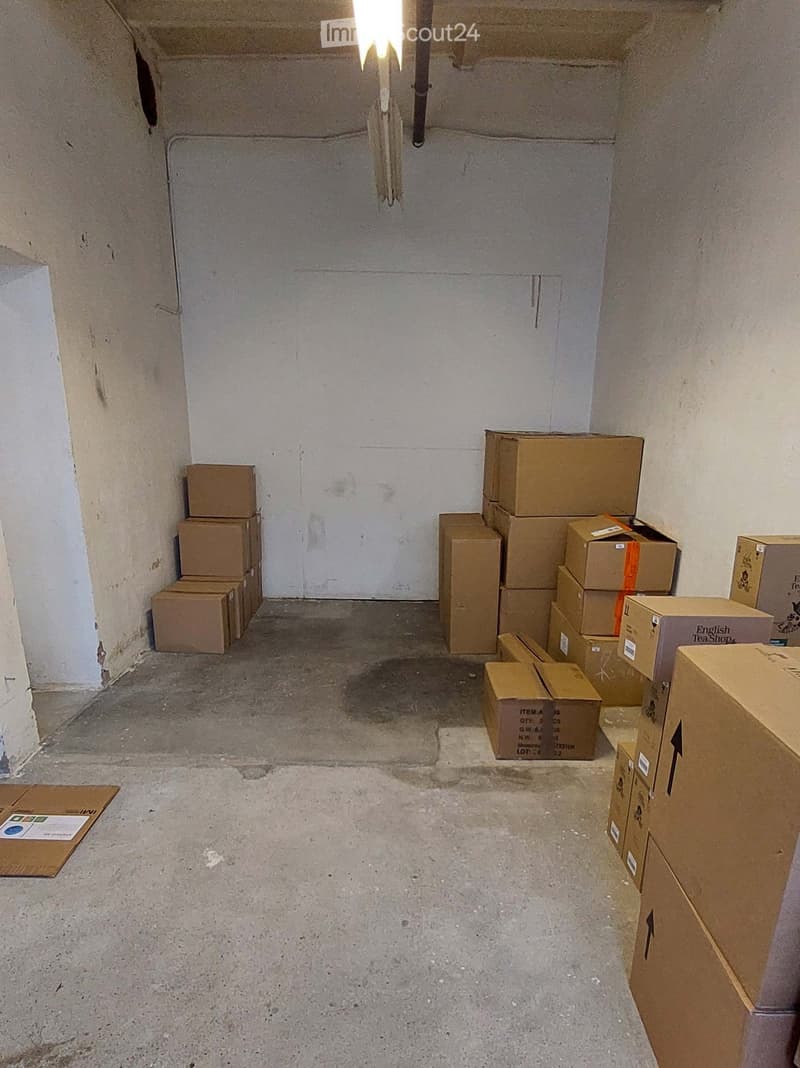 Empty room with concrete floor and bare walls, several cardboard boxes stacked against the walls.