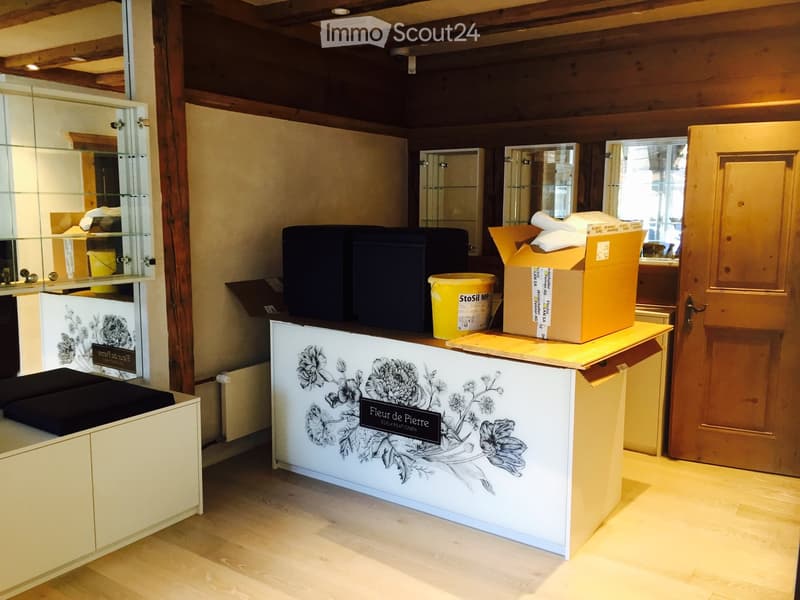 Reception area with a white reception desk featuring floral artwork, several stools, and a cardboard box on top.