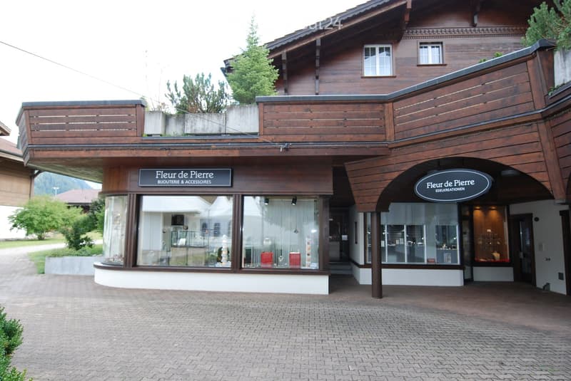 A two-story wooden building with a balcony and large windows, featuring a storefront with glass display windows and signage reading "Fleur de Pierre" and "Edelkreationen".
