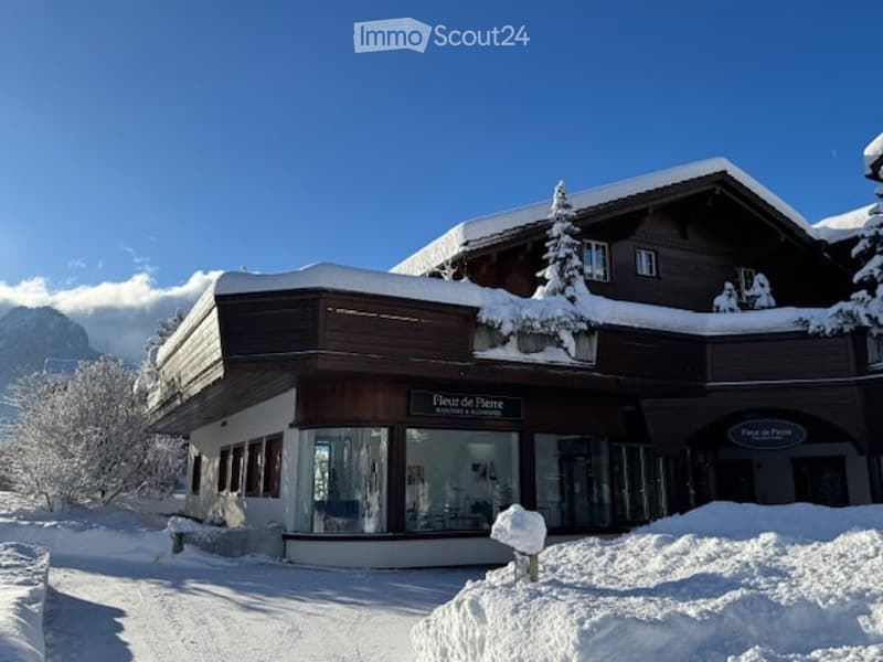 A large, multi-story wooden building with snow-covered roof and surrounding snow-covered trees, likely a ski lodge or resort.