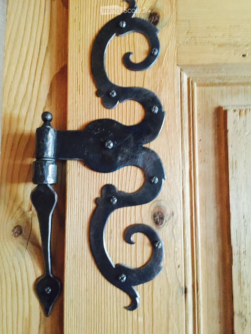 Close-up of a decorative black metal door handle with ornate design mounted on a light wooden door.