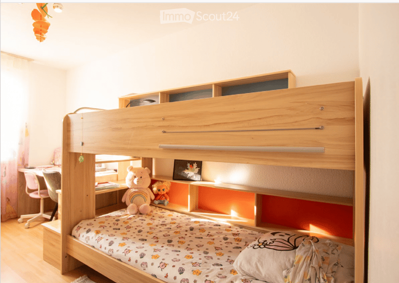 Bright, modern bedroom with a wooden bunk bed, a small desk with a chair, and colorful toys on the lower bunk.