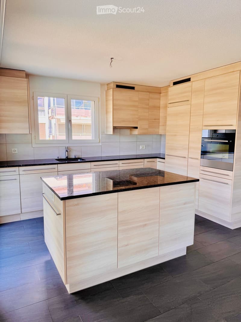 Modern kitchen with light wooden cabinets, black granite countertop, stainless steel sink and oven, and a central island.