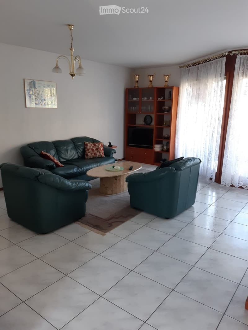 Living room with a dark green leather sofa, armchair, coffee table, bookshelf, and a chandelier light fixture.
