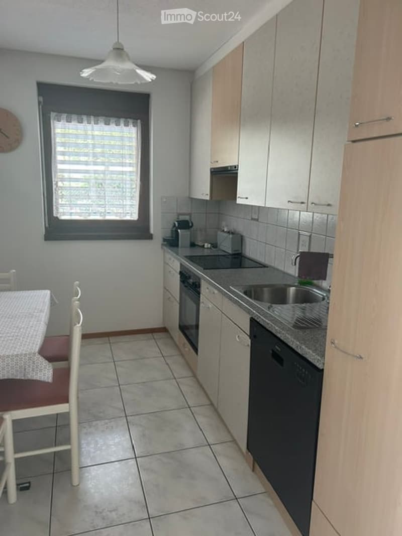 Modern kitchen with white cabinets, granite countertop, stainless steel sink, dishwasher, and oven. A small dining area with a table and chairs is visible.