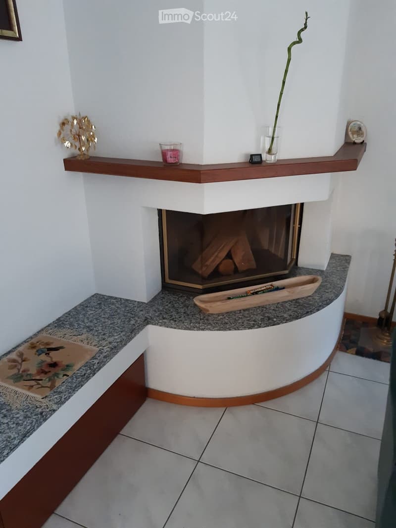 Modern fireplace with wooden shelf, candle, vase, decorative items, and a wooden tray on the mantle.