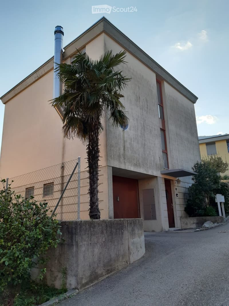 Two-story building with beige and grey exterior, red doors, and a palm tree in front.