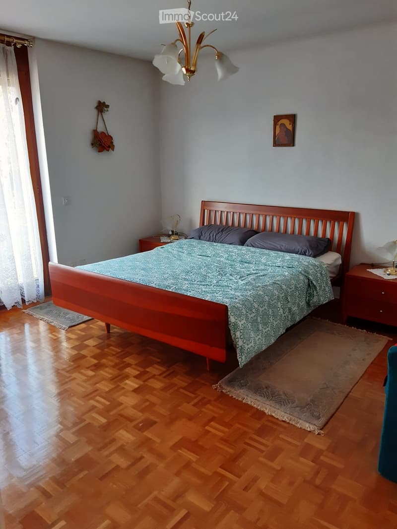 Cozy bedroom with wooden flooring, a wooden bed with a blue patterned duvet, nightstands, a hanging flower decoration, and a framed picture on the wall.