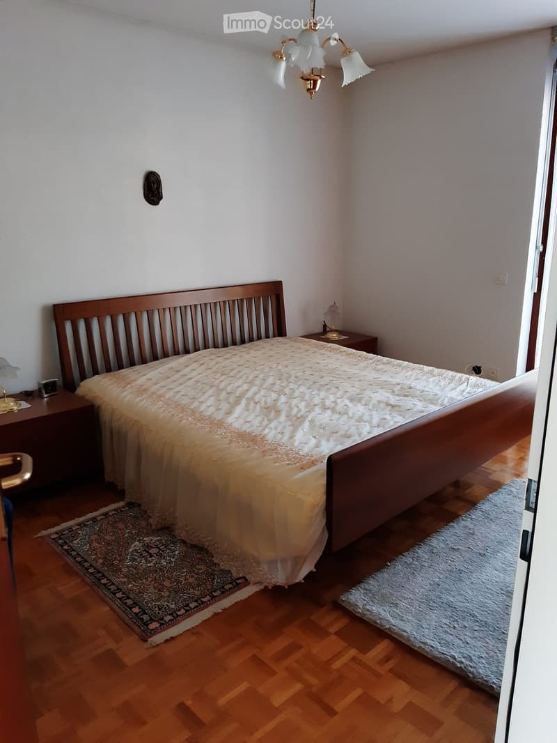 Cozy bedroom with wooden flooring, a large bed with a patterned bedspread, two nightstands with table lamps, and two rugs on the floor.