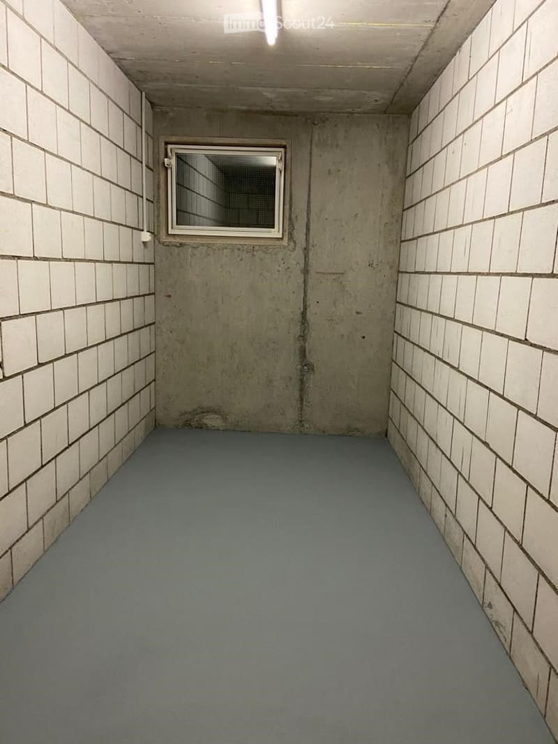 Empty room with concrete walls, tiled sections, and a small window. Blue flooring and exposed concrete surfaces.