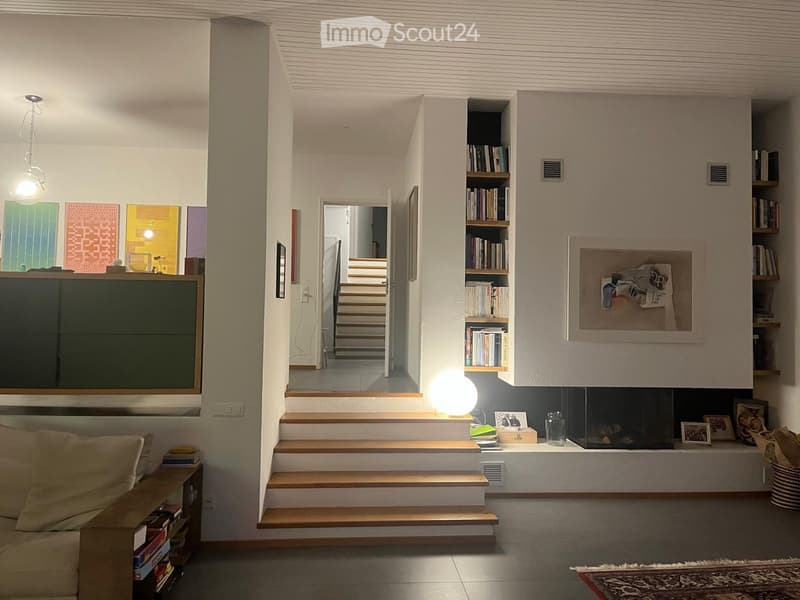 Modern living room with a fireplace, bookshelf, sofa, and a staircase leading to another level.