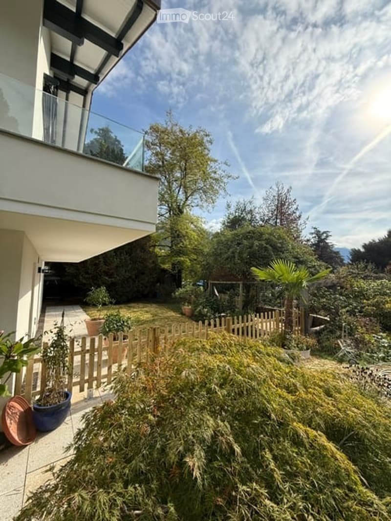 Garden area with a wooden fence, potted plants, and a modern balcony overlooking the space.