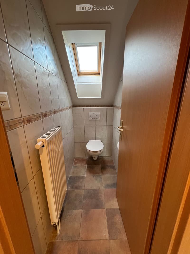 small bathroom with white toilet, small tiled floor, white tiles on the wall, window, radiator