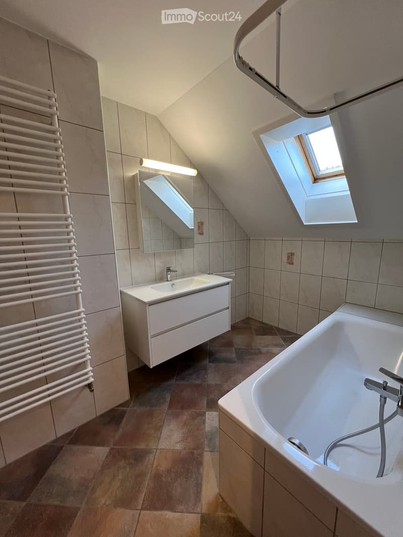 small attic bathroom with a bathtub, sink and a shower with skylights, white tiled walls and floors