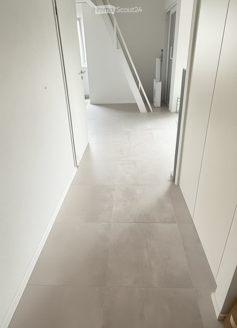 Clean, modern hallway with light grey tiled flooring and white walls. Features a staircase leading upwards and several doors along the sides.
