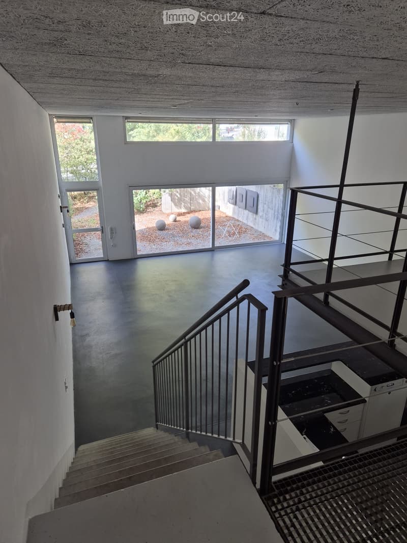 Modern, minimalist hallway with a staircase leading upwards, large windows, and a view of an outdoor area with spherical sculptures.