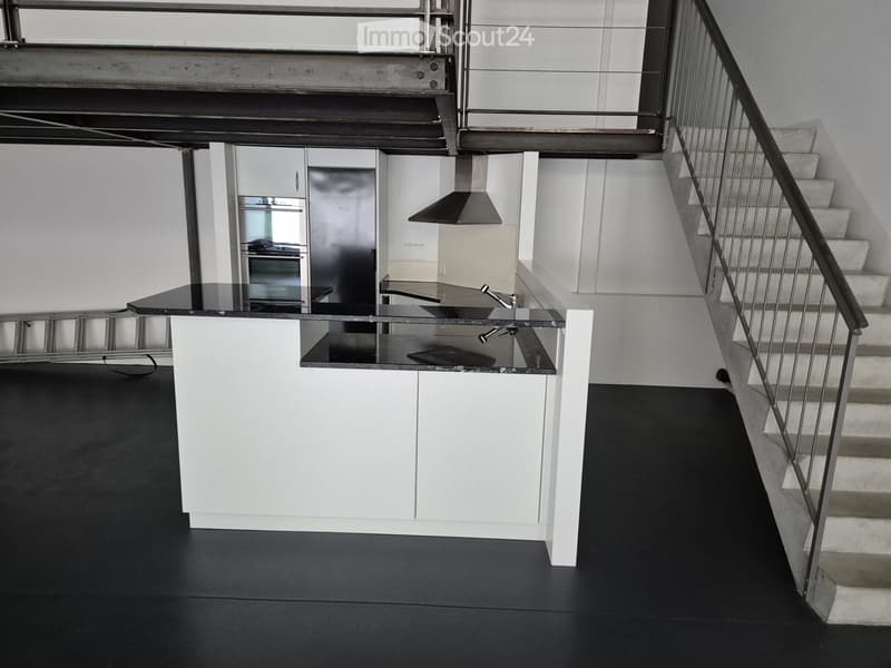 Modern kitchen with white cabinets, black countertops, stainless steel appliances, and a staircase leading upwards.