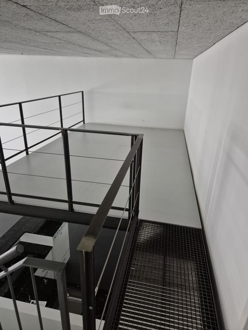 Modern interior staircase with metal railings and a grid-patterned step surface, leading to an upper level with a concrete floor and white walls.