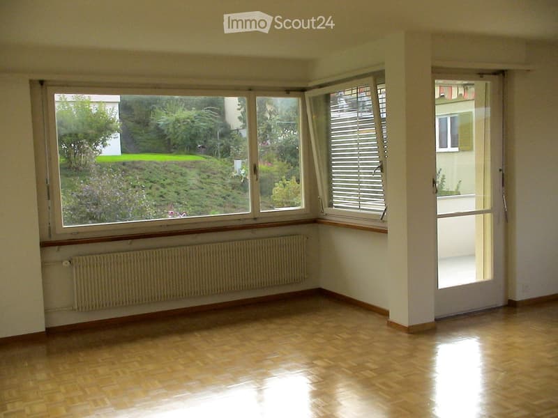 Empty room with wooden flooring, large windows, radiator, and a door leading outside.