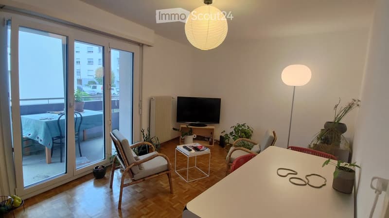 Bright living room with wooden flooring, large sliding glass doors leading to a balcony, a sofa, a chair, a small table, a television, and a floor lamp.