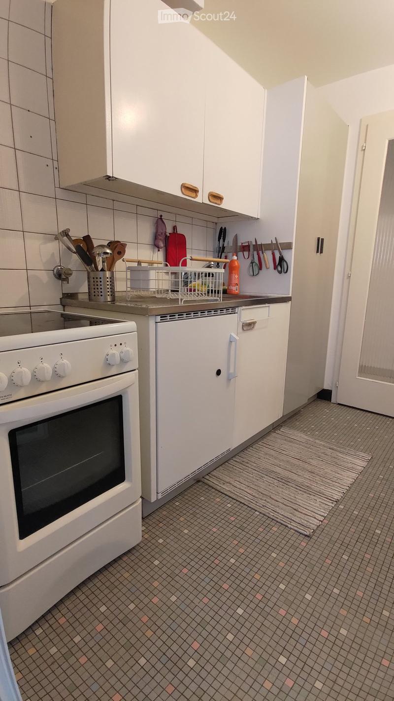 Modern kitchen with white cabinets, tiled walls, and a tiled floor. Features an oven, dishwasher, and various kitchen utensils.