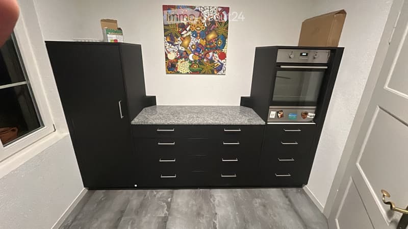Modern kitchen with black cabinets, a grey countertop, and a built-in oven. A colorful abstract painting hangs on the wall.