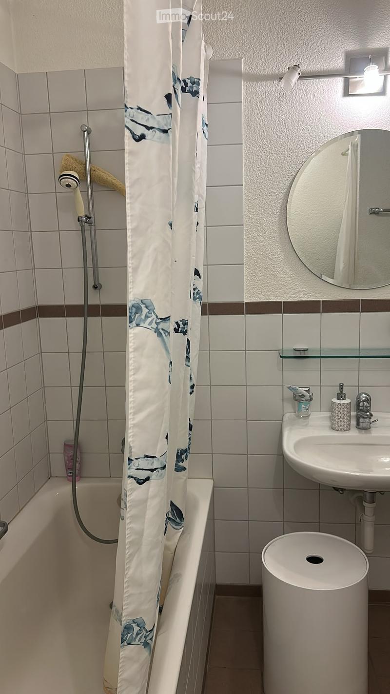 Bathroom with a bathtub, shower curtain, sink, mirror, and toilet. The walls are tiled with white tiles and brown accents.