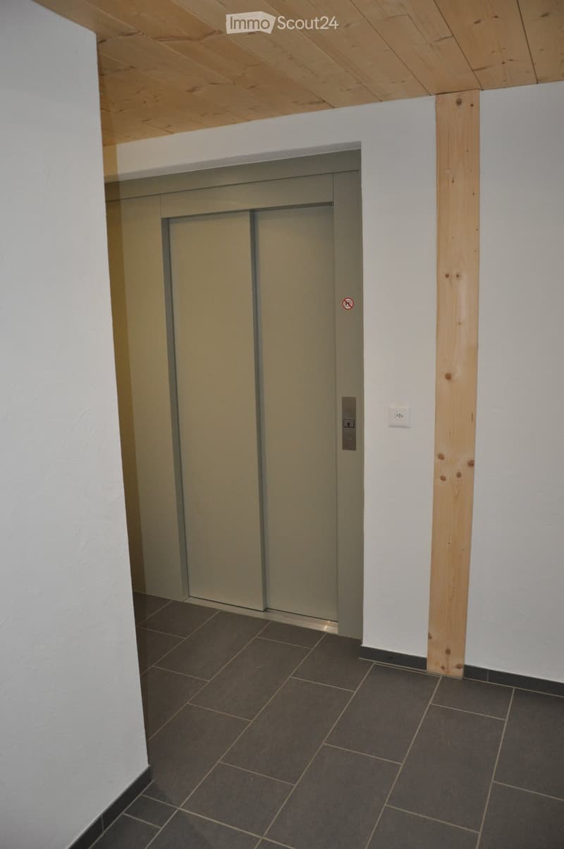A modern hallway with a closed elevator door, dark tiled floor, and white walls with wooden trim.