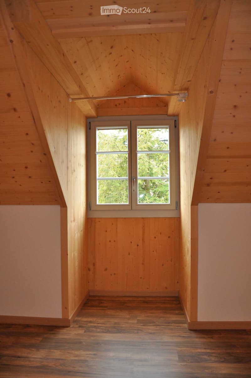 Empty attic space with wooden walls, ceiling, and floor, featuring a large window and a built-in closet with sliding doors.