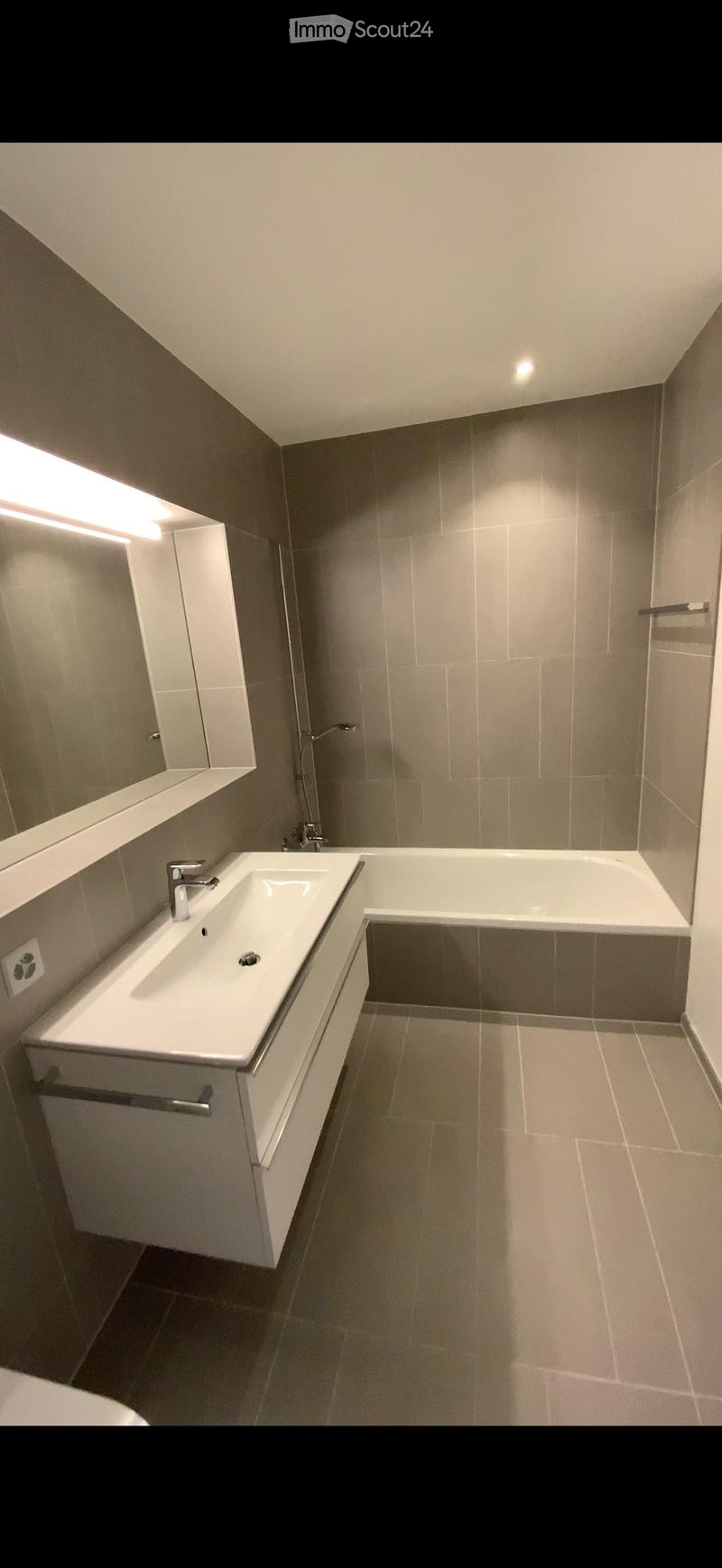 Modern bathroom with a white sink, bathtub, and mirrored cabinet. Features sleek fixtures and neutral tones.