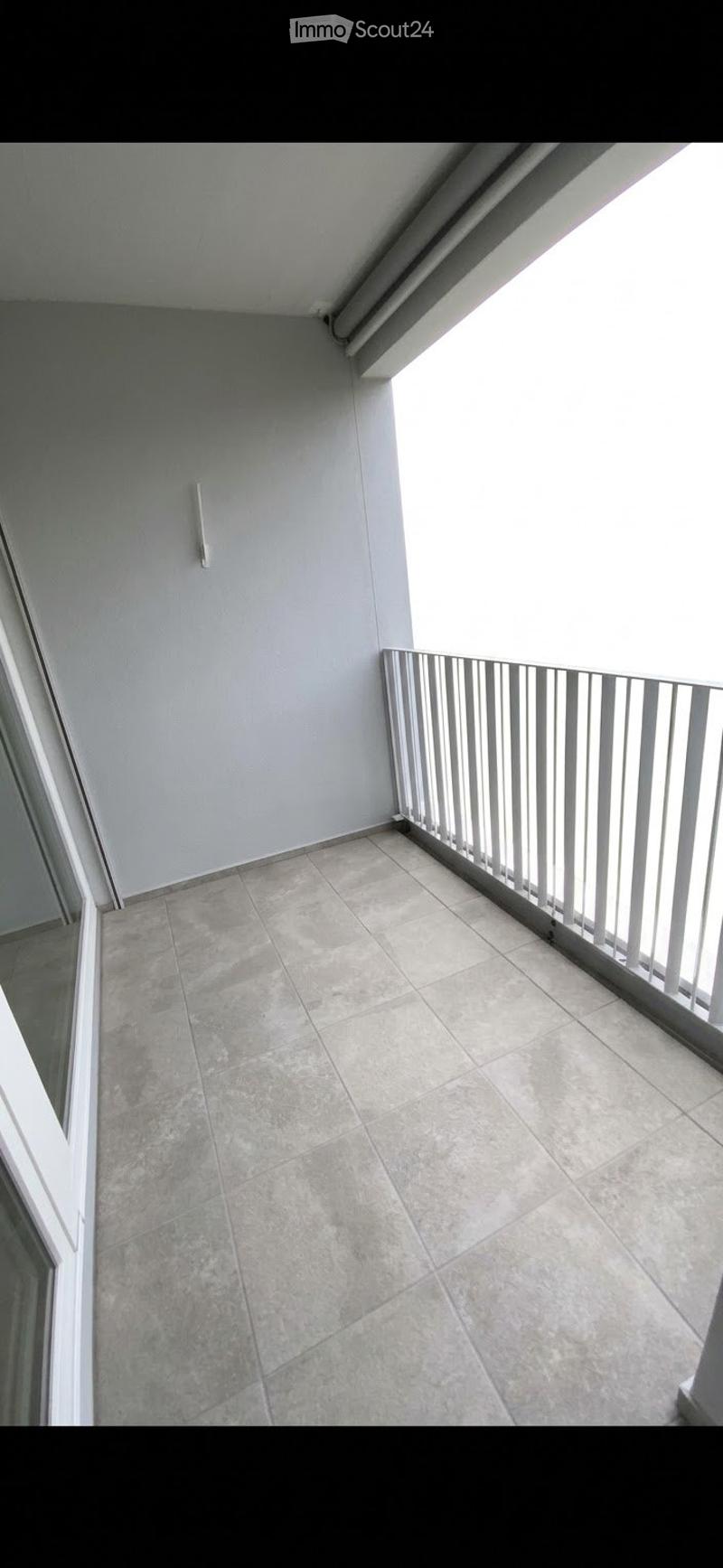 Empty balcony with tiled floor and white metal railing, featuring a light fixture on the wall.