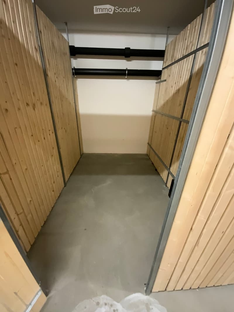 Empty hallway with wooden panel walls, concrete floor, and exposed pipes on the ceiling.