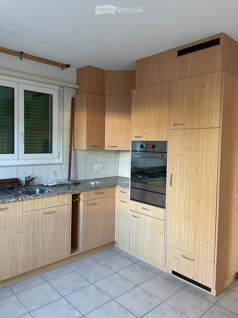 Modern kitchen with light wooden cabinets, granite countertop, stainless steel oven, and sink.