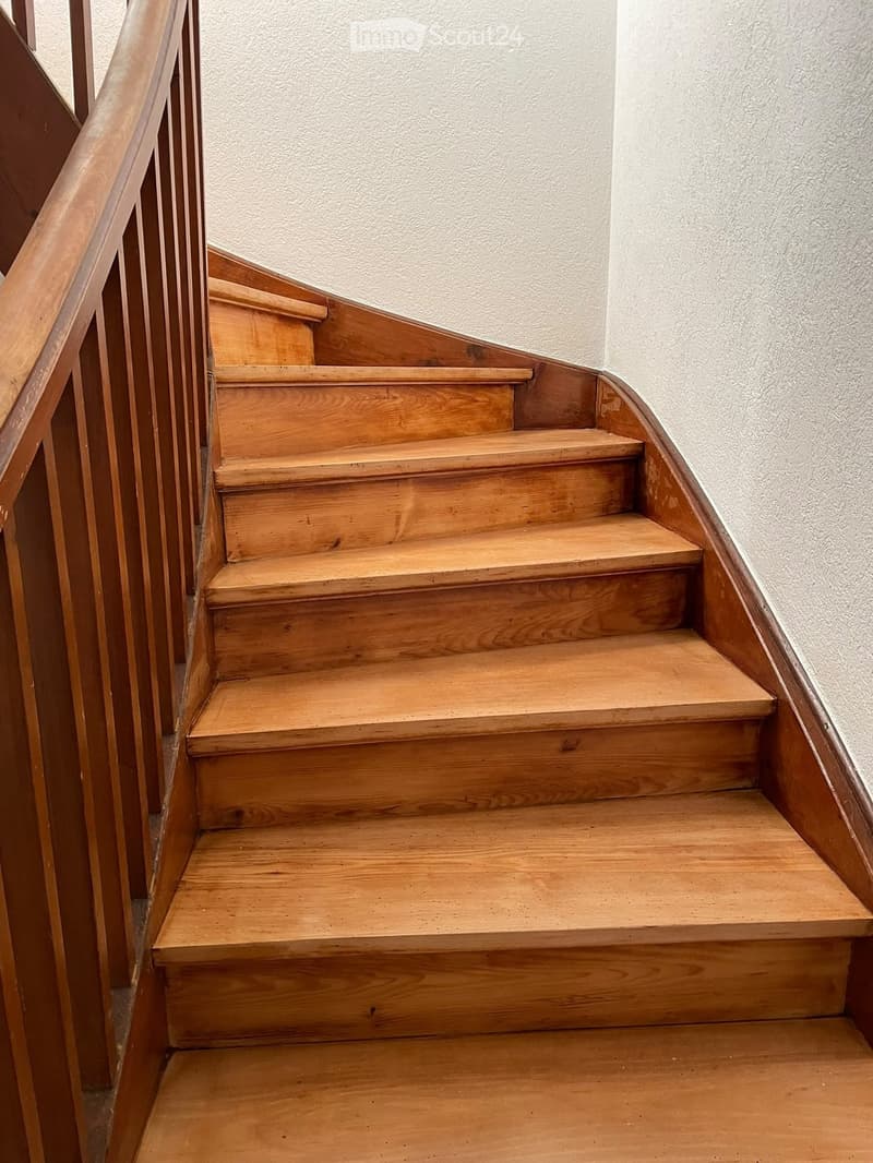 Wooden staircase with a handrail, light-colored walls, and a curved design.