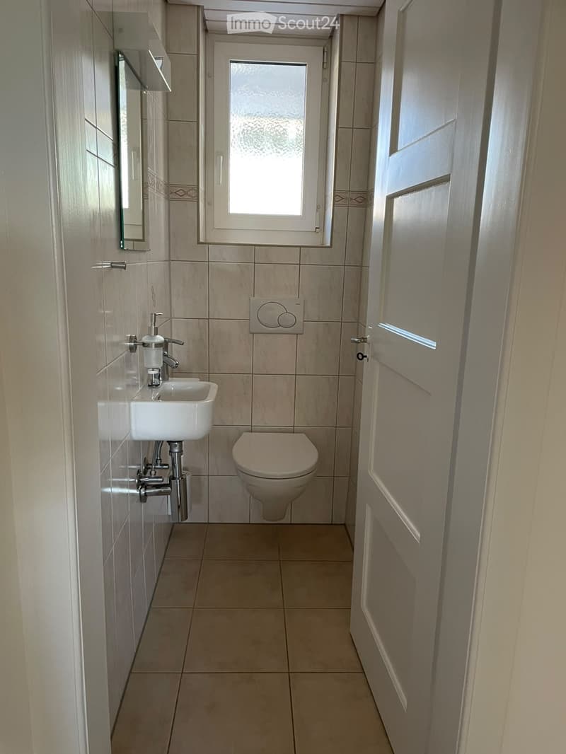 Small bathroom with beige tiles, a white sink, a toilet, and a mirror on the wall.