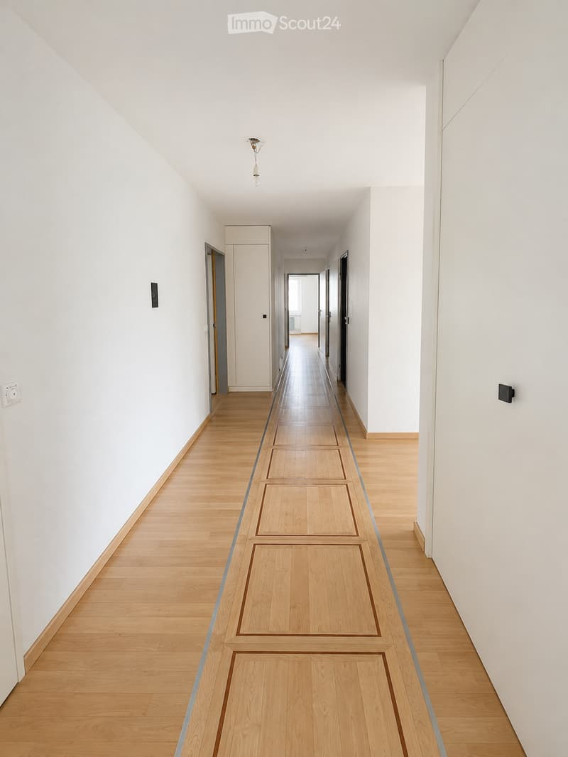 A clean, modern hallway with light wooden flooring and white walls, featuring several doors and a single ceiling light fixture.