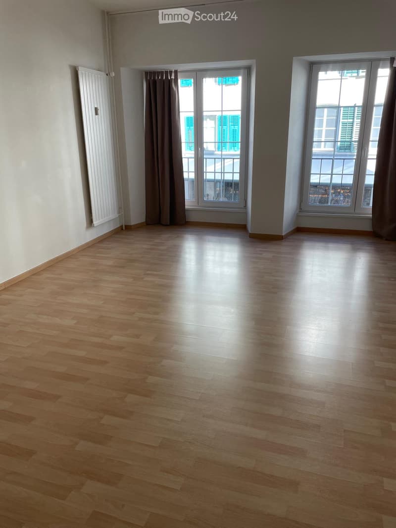 Empty room with wooden flooring, large windows, and a sliding glass door leading to a balcony.