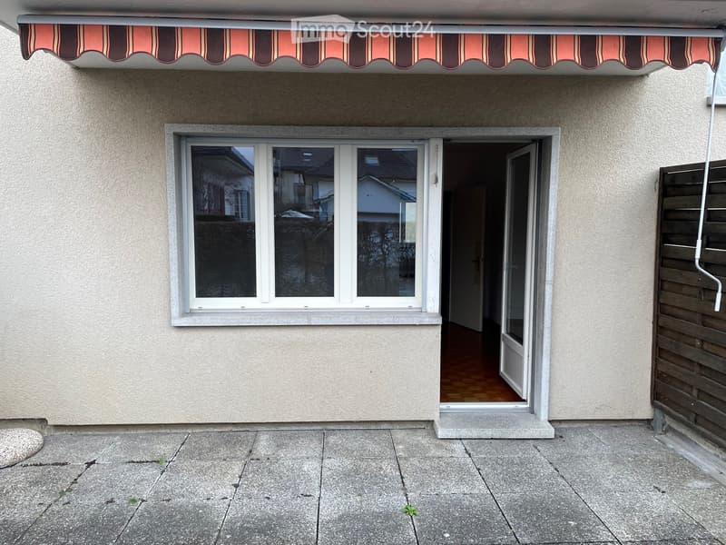 Balcony with striped awning, large window, and wooden fence.