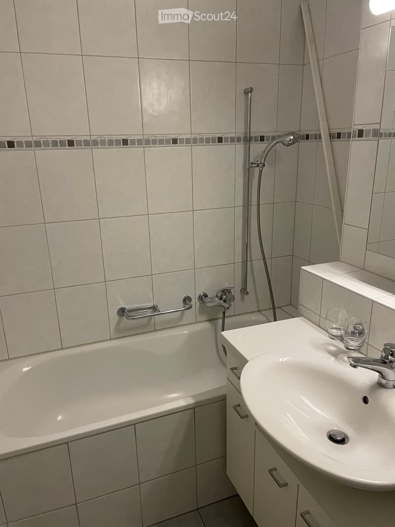 Bathroom with a white bathtub, a sink with a faucet, a mirror, and two cups on the sink counter.