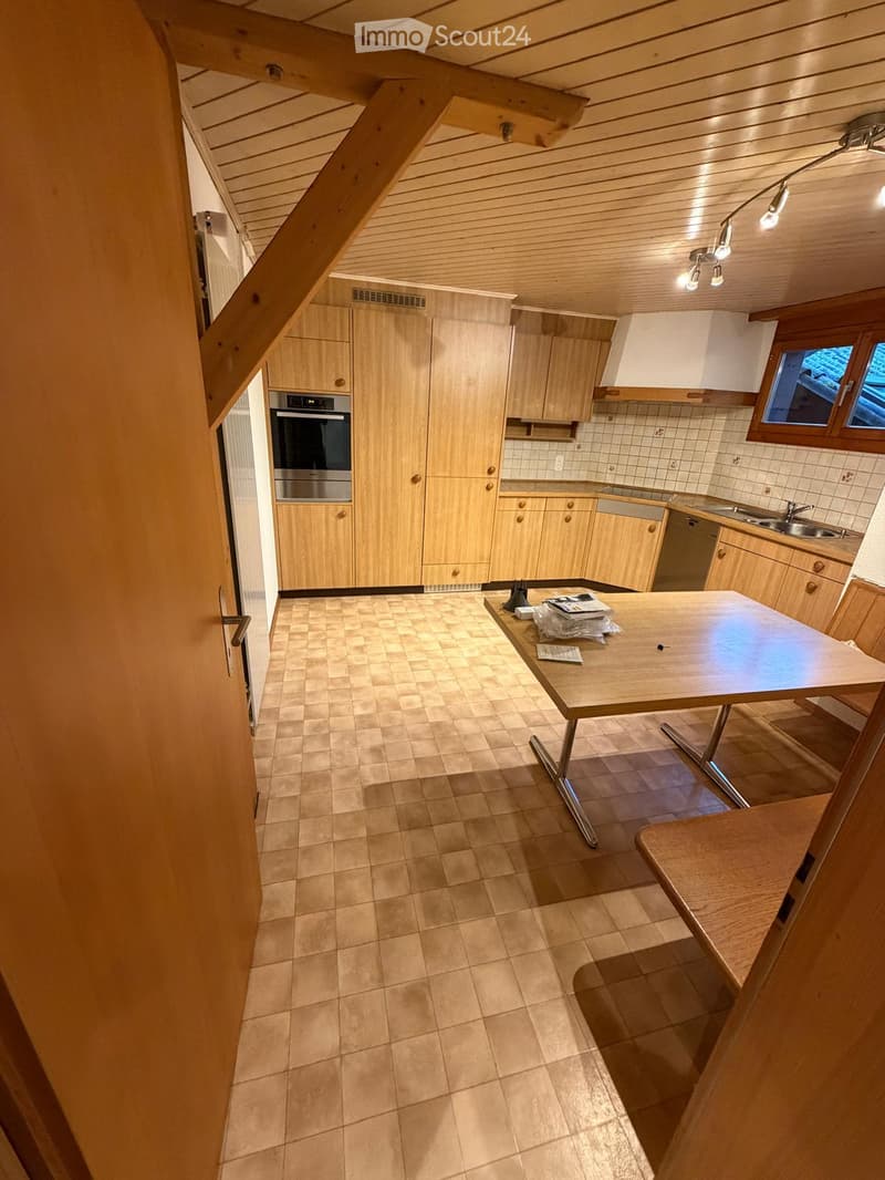 Bright kitchen with wooden cabinets, tiled floor, and a central table. Features an oven, sink, and faucet.