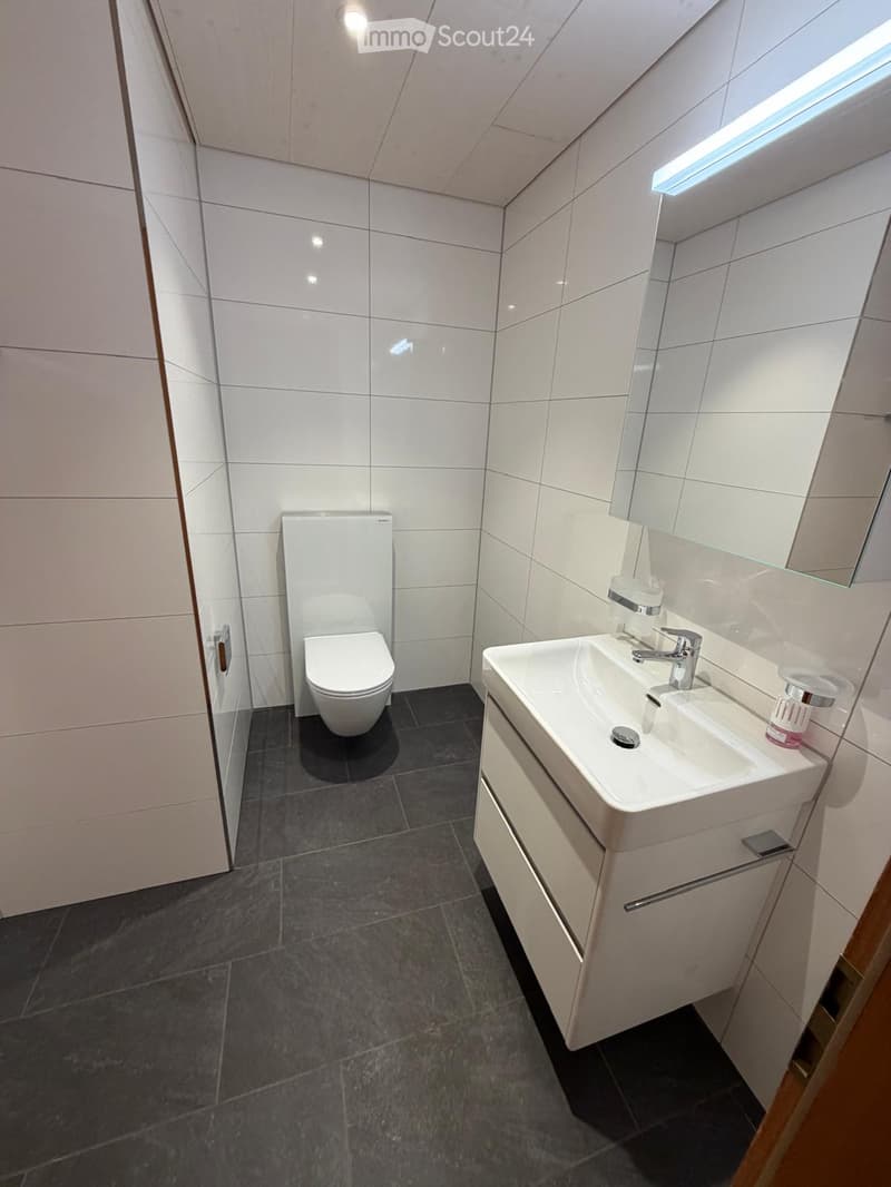 Modern bathroom with white tiles, a toilet, a sink with a faucet, a mirror, and a white cabinet.