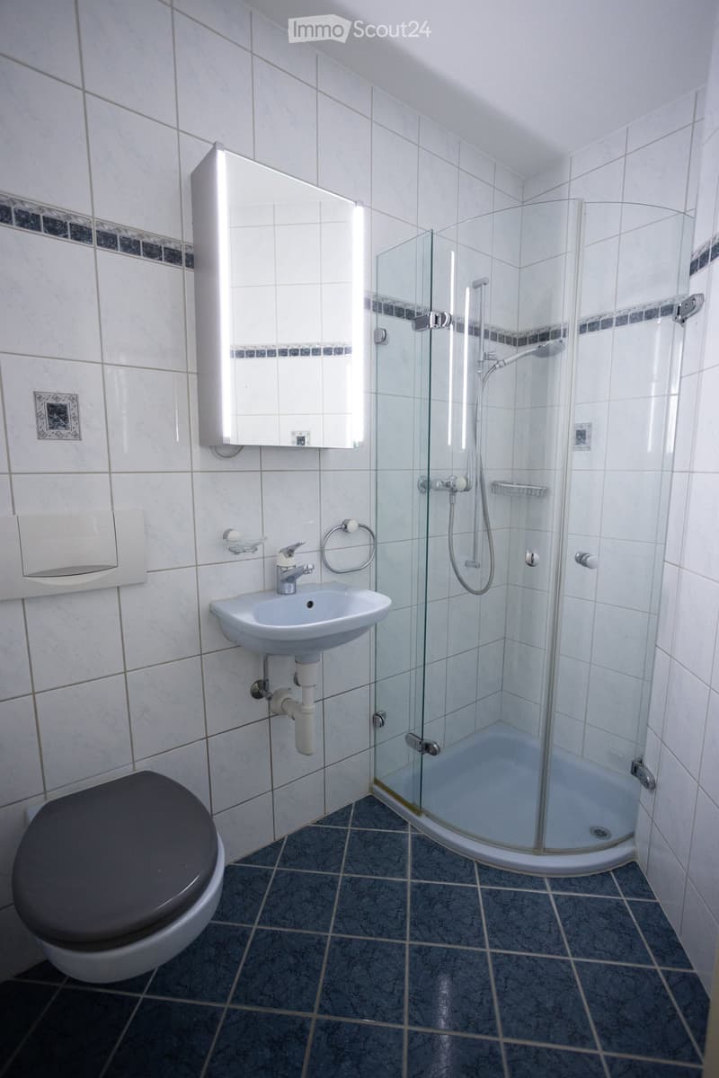 Modern bathroom with white tiles, a toilet, a sink with a mirror, and a glass-enclosed shower stall.