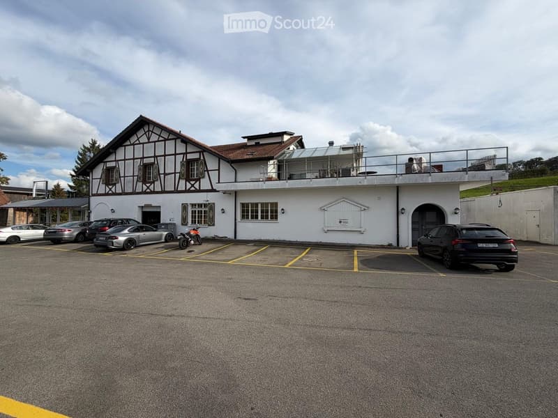 Two-story building with a balcony, parking area with several cars, and a motorcycle.