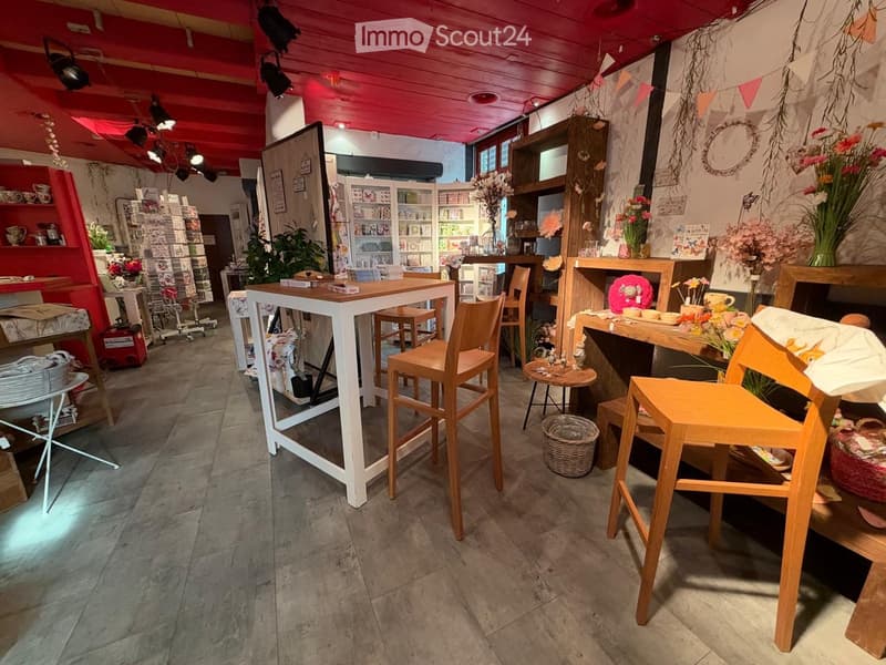 A cozy, well-lit shop interior with wooden tables, chairs, shelves filled with items, and decorative vases.
